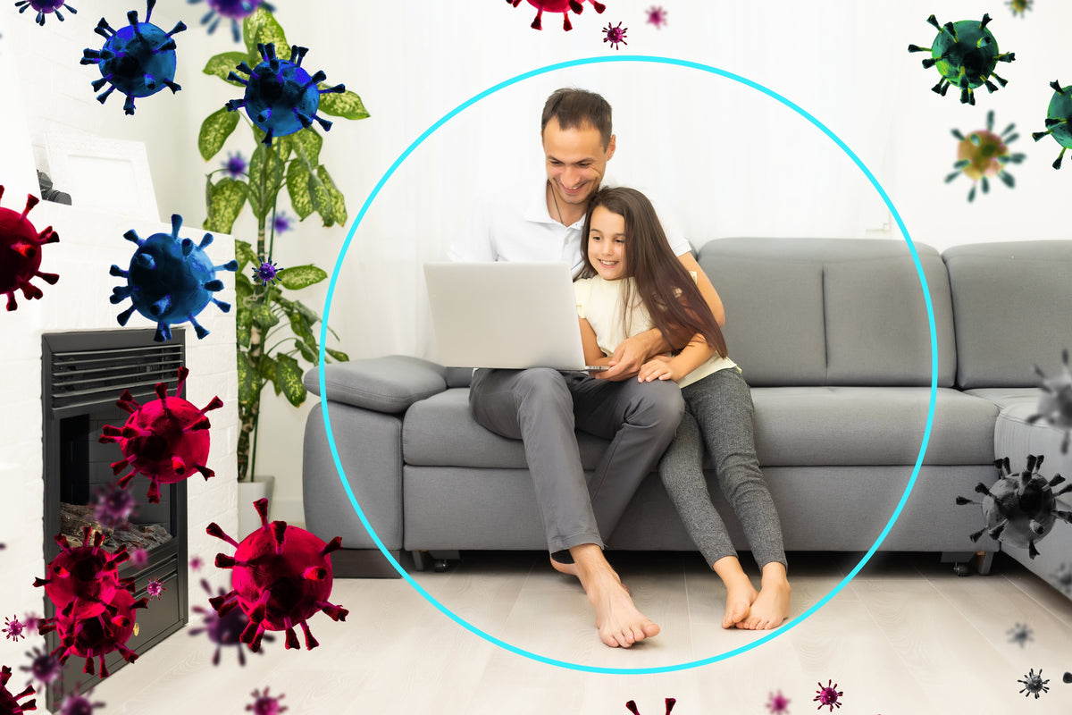 Father and daughter on a sofa inside a protective shield while virus particles stay outside